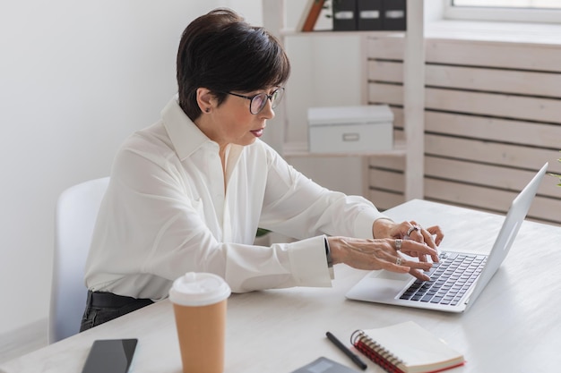 Mujer hermosa de mediana edad sonriendo mientras trabaja con una computadora portátil en el concepto de trabajo de oficina y gerente