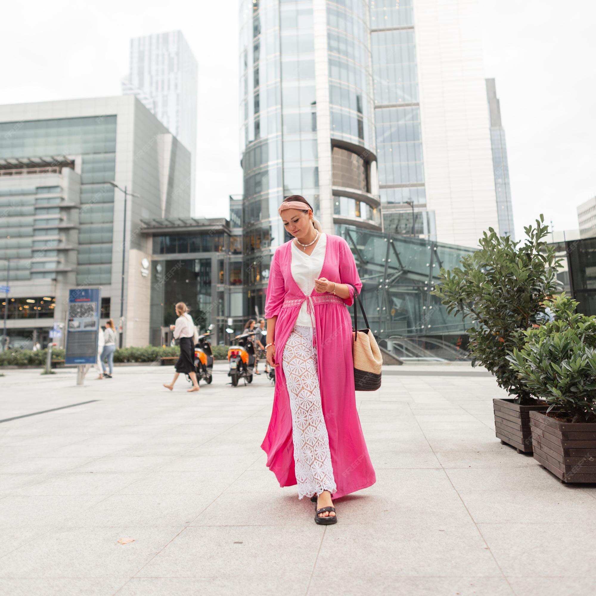 Mujer de moda modelo de talla grande con ropa verano elegante con vestido rosa y pantalones de encaje con bolso camina en ciudad moderna Foto Premium