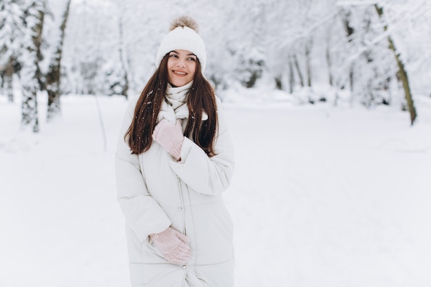 Una mujer hermosa y de moda con ropa blanca y abrigada caminando en clima nevado.