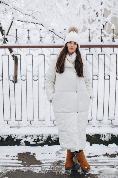 Una mujer hermosa y de moda con ropa blanca y abrigada caminando en clima nevado.