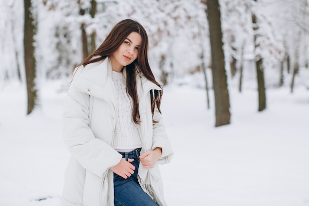 Una mujer hermosa y de moda con ropa blanca y abrigada caminando en clima nevado.