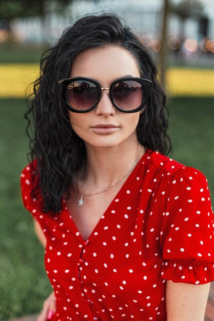 Mujer hermosa modelo con el pelo rizado en gafas de sol de moda y vestido rojo en la calle