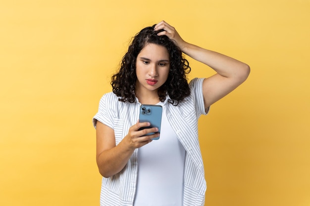 Foto mujer hermosa pensativa usando teléfono celular pensando qué responder mantiene la mano en la cabeza