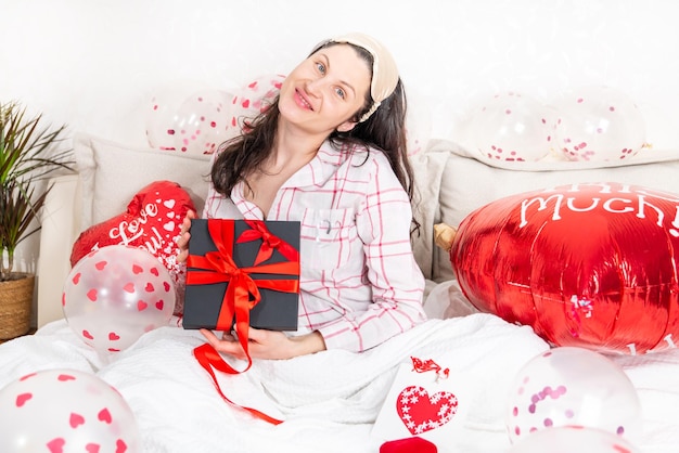 Una mujer hermosa en pijama rosa con un globo en forma de corazón yace en la cama en casa