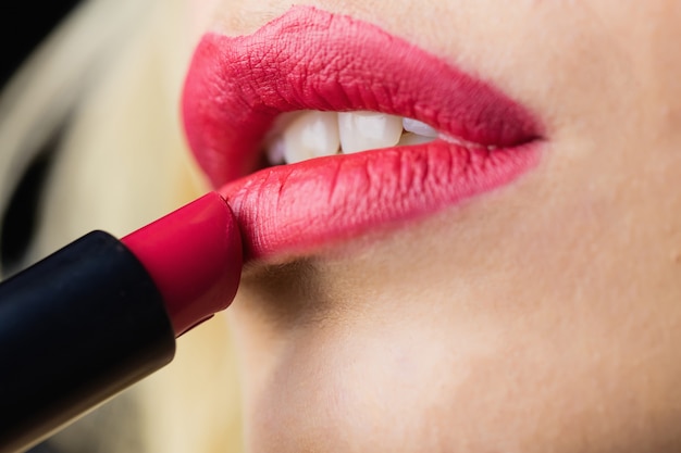 Mujer hermosa que aplica el lápiz labial rojo en los labios