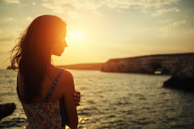 Mujer hermosa que mira en la distancia la puesta del sol contra el cielo.