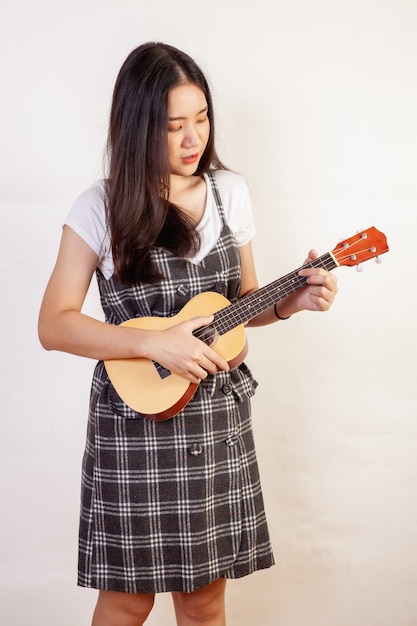 Mujer hermosa que presenta tocando el ukelele en una pared blanca.