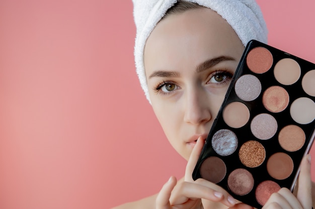 Mujer hermosa que sostiene la paleta de sombras de ojos coloridas en fondo rosado. Copia espacio