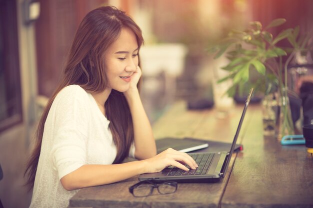 Mujer hermosa que usa la computadora portátil en el café mientras que bebe el café, concepto relajante del día de fiesta.