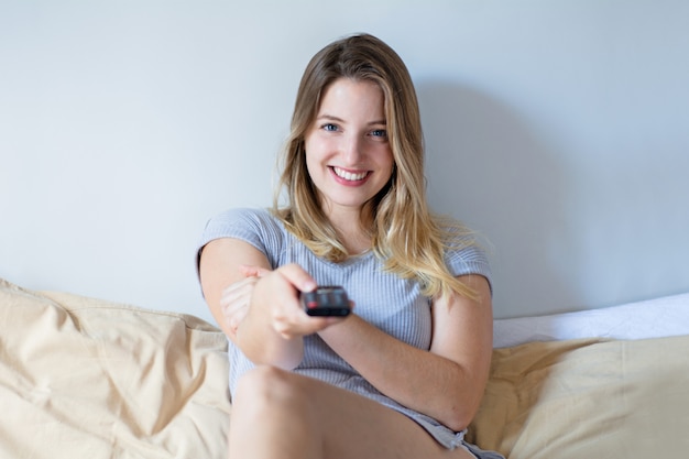 Mujer hermosa que ve la TV y que miente en cama.