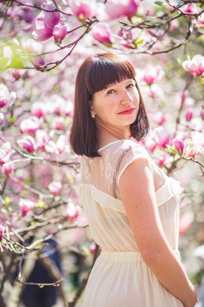 Mujer hermosa entre ramas de la magnolia en primavera en parque.