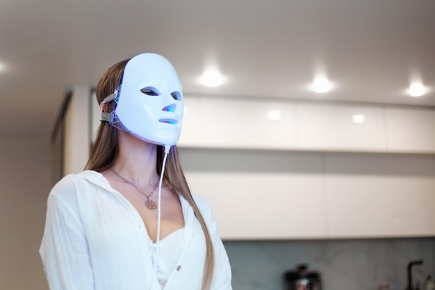 Mujer hermosa recibiendo un tratamiento de mascarilla de terapia de luz dirigida para su cara en casa