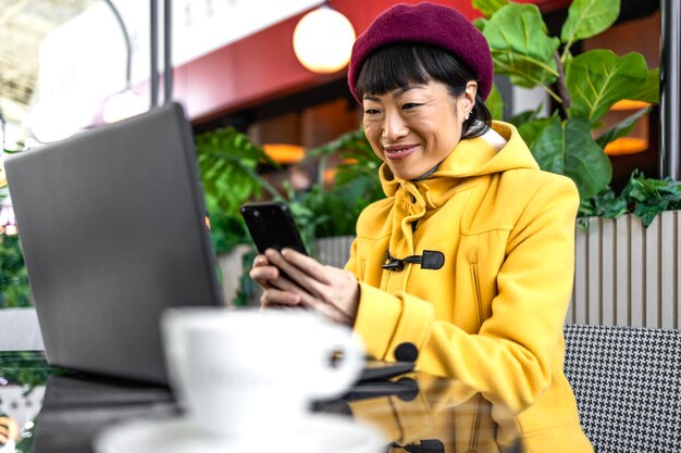 Una mujer hermosa relajándose en un café usando un teléfono móvil y una computadora portátil