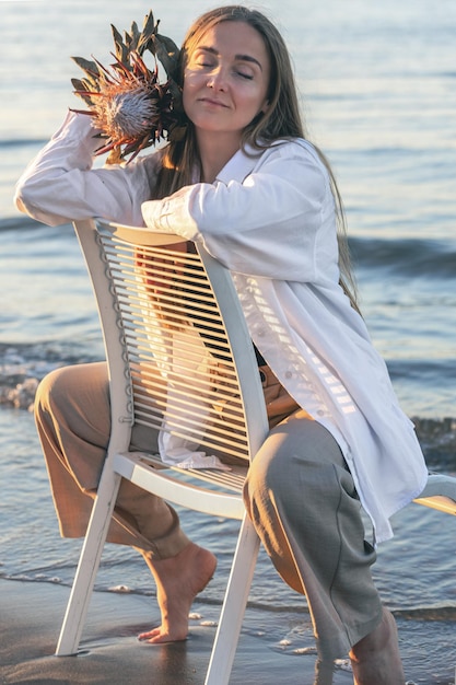 Una mujer hermosa se sienta en una silla cerca del mar.