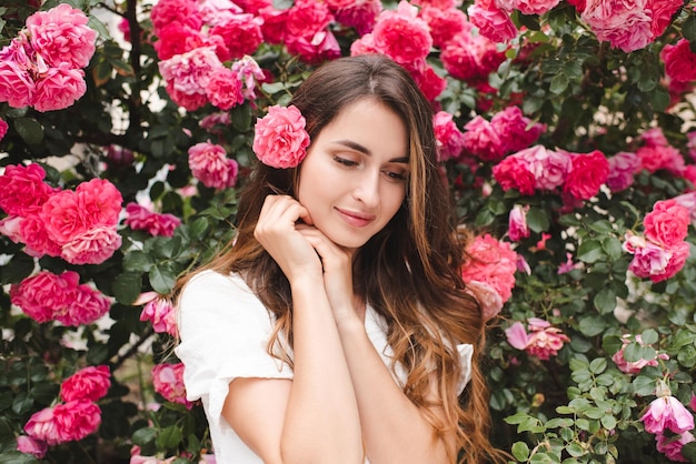 Mujer hermosa sonriente con cabello largo y rubio y flor de rosa sobre el fondo de la naturaleza en flor al aire libre