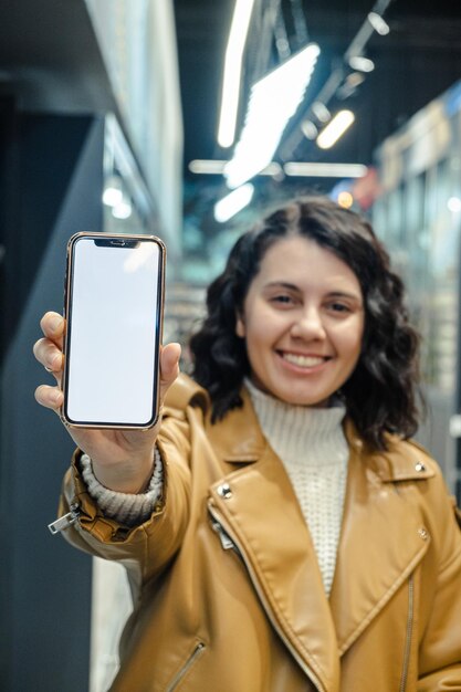 Una mujer hermosa sostiene un teléfono con una pantalla blanca en blanco en una tienda de comestibles