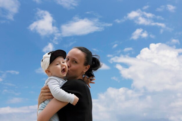 Una mujer hermosa y su pequeño hijo se abrazan fuertemente contra un cielo azul con nubes Retrato de verano de madre e hijo en el Día de la Madre Foto de alta calidad