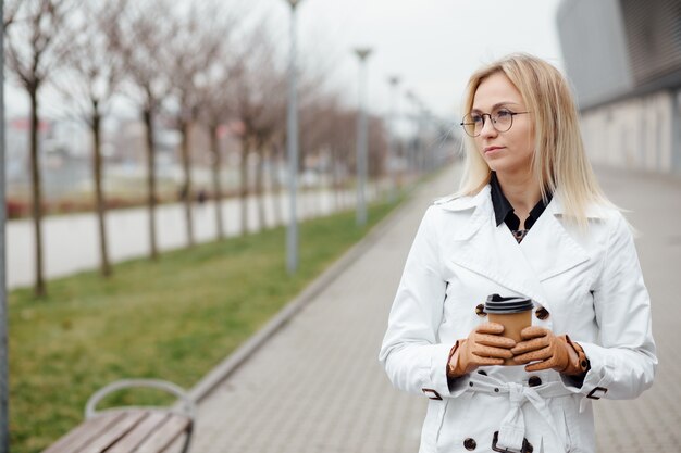 Mujer hermosa con la taza de café cerca del edificio de oficinas.