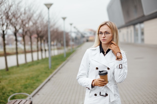 Mujer hermosa con la taza de café cerca del edificio de oficinas.