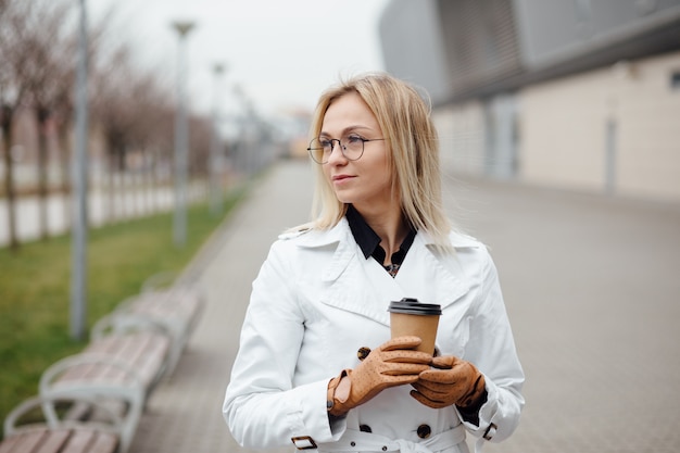 Mujer hermosa con la taza de café cerca del edificio de oficinas.