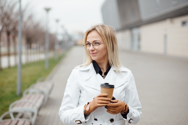 Mujer hermosa con la taza de café cerca del edificio de oficinas.