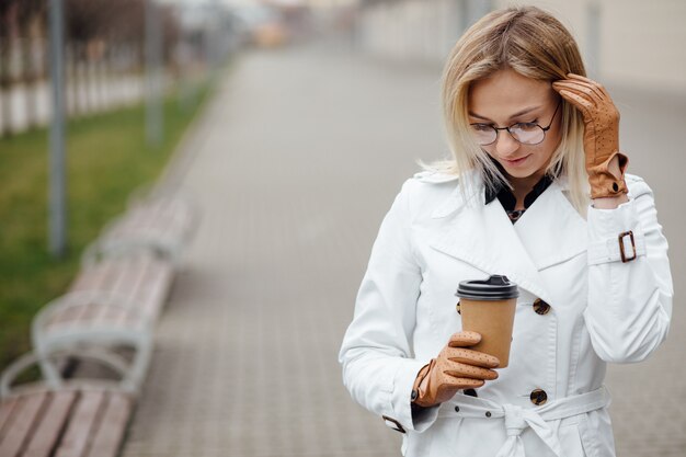 Mujer hermosa con la taza de café cerca del edificio de oficinas.