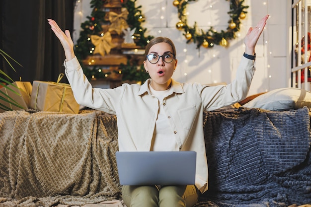 Una mujer hermosa trabaja en casa en las vacaciones de Año Nuevo, usa ropa cómoda para el hogar, mira una computadora portátil, trabaja de forma remota para el estado de ánimo de invierno de Año Nuevo a cuadros.