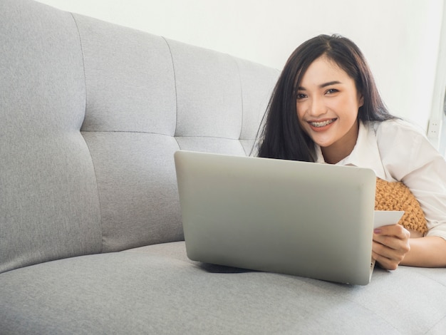 Mujer hermosa en un vestido blanco, jugando una computadora de computadora portátil en el sofá.