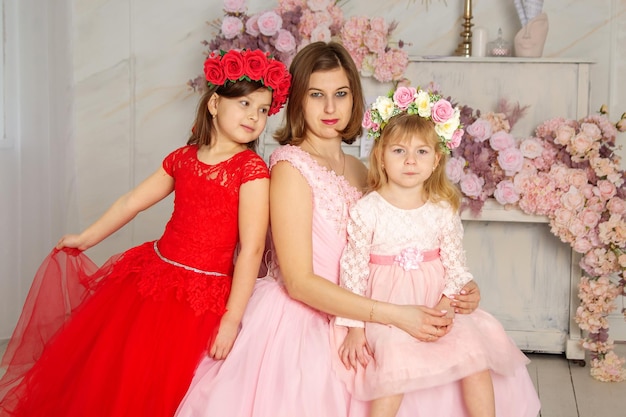 Una mujer hermosa con un vestido largo rosa en un salón con flores es fotografiada con sus hijas que tienen coronas de flores en la cabeza Las niñas son lindas SESIÓN FOTOGRÁFICA de primavera Familia