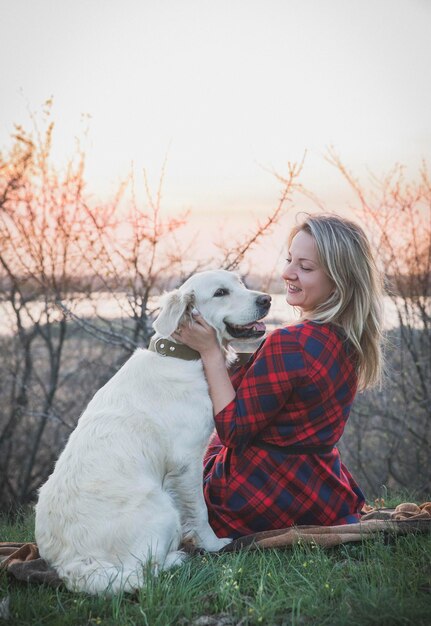 Foto mujer hermosa en un vestido con un perro al atardecer en el bosque