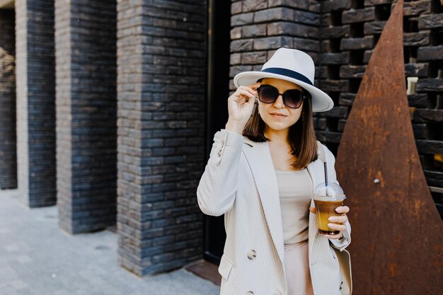 Mujer hermosa yendo a una reunión con café frío caminando por la calle Retrato de una mujer de negocios exitosa sosteniendo una taza de bebida fría en la mano de camino al trabajo en la calle de la ciudad