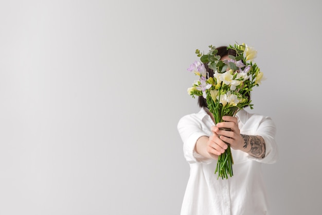 Mujer con hermosas flores de fresia en superficie clara