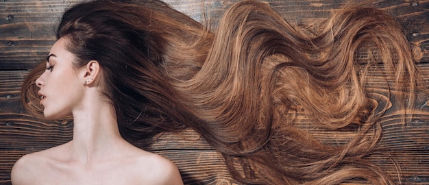 Mujer con hermoso cabello largo sobre fondo de madera. Pelo largo. Cortes de pelo de moda. Peluquería de belleza.