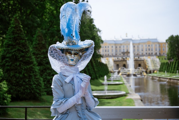 Mujer con un hermoso vestido de carnaval azul y una máscara veneciana en el parque en un día soleado