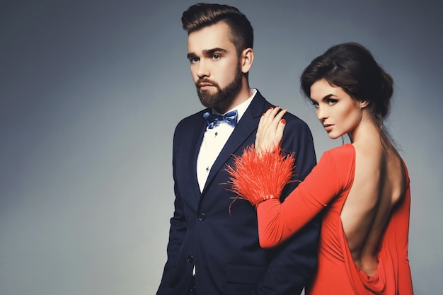 Mujer en hermoso vestido rojo y hombre vestido con traje clásico azul con pajarita.