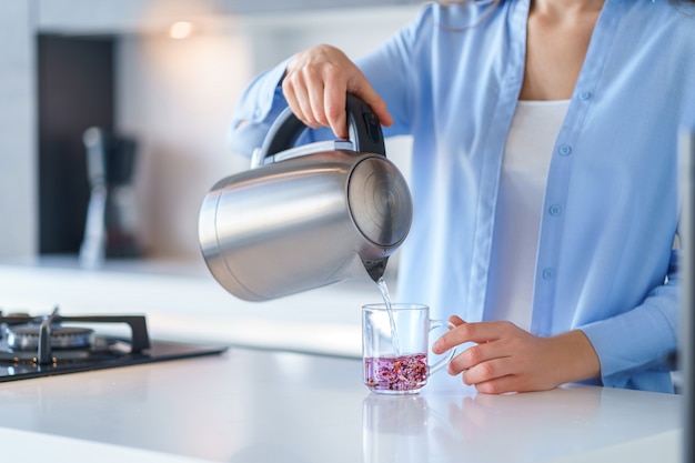 Foto mujer con hervidor eléctrico de metal plateado para hervir agua y hacer té en casa. electrodomésticos de cocina para hacer bebidas calientes