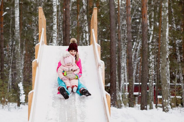 Mujer con hija se desliza por una colina de madera helada en un día de nieve.