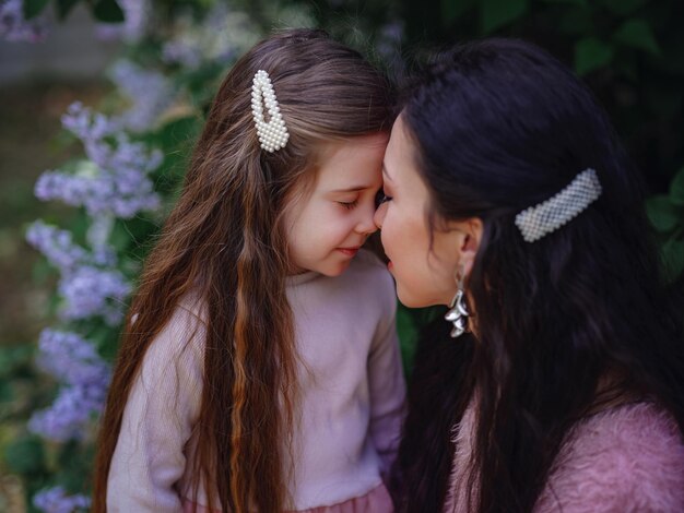 Mujer con hija en hermosos vestidos de color rosa que se divierten al aire libre en el jardín lila de primavera. Mamá y niño sonriendo y abrazándose. Vacaciones familiares y convivencia. ¡Feliz día de la madre!