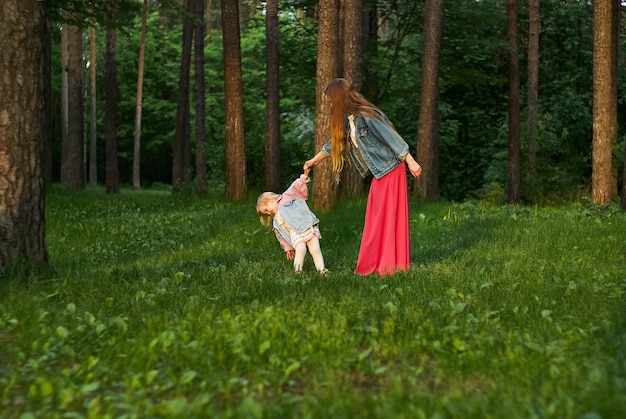 Mujer con hija pequeña caminar y bailar en el césped en el parque