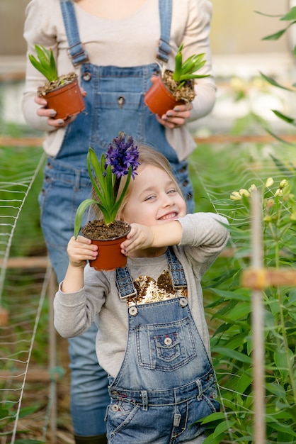 Una mujer con una hija pequeña mantiene flores en macetas en un invernadero en primavera.