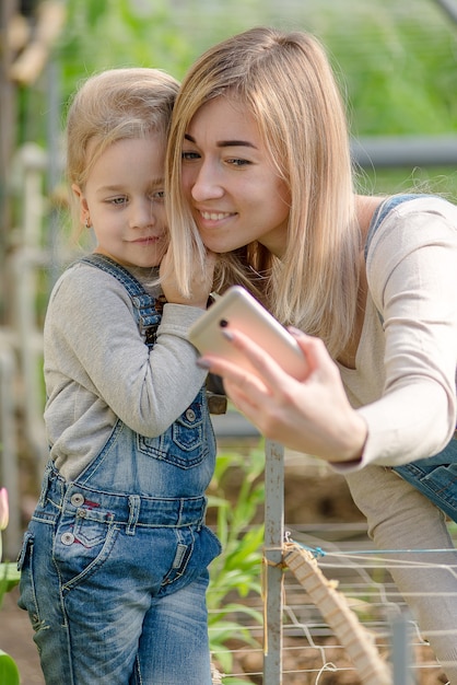 Una mujer con una hija pequeña se toma un selfie en un invernadero con flores en primavera.