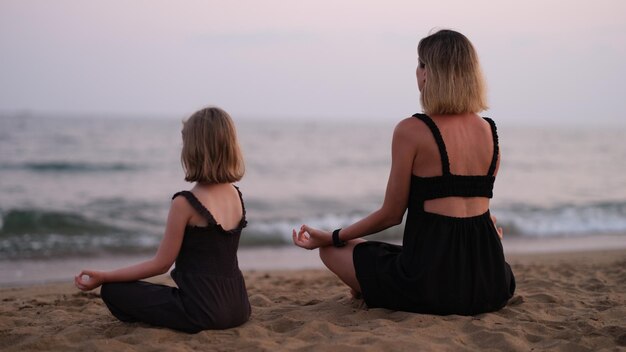 Mujer con hija en la playa está haciendo yoga