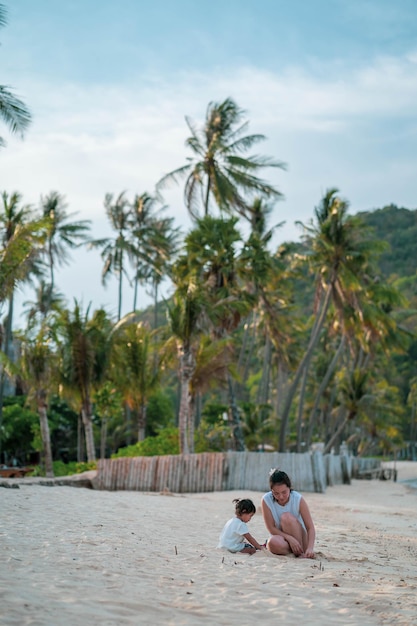 Mujer con hija sentada en la playa contra el cielo