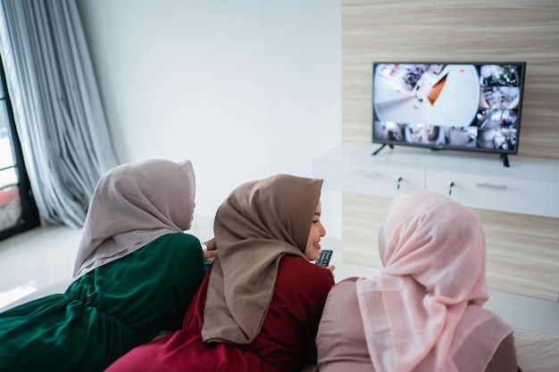 Mujer hijab asiática con amigos acostada en la cama disfruta viendo la televisión