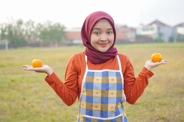 Mujer hijab asiática con delantal sosteniendo una fruta naranja