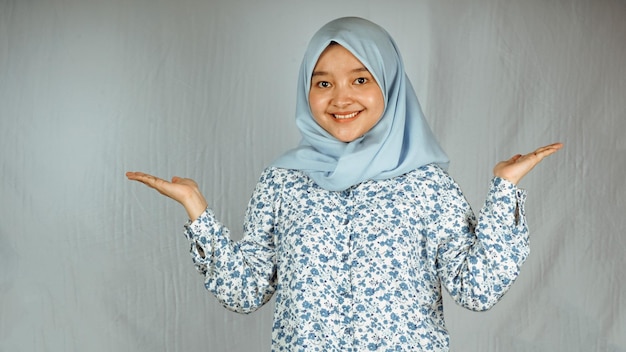 Mujer hijab asiática sonriente apuntando hacia arriba y mirando a la cámara