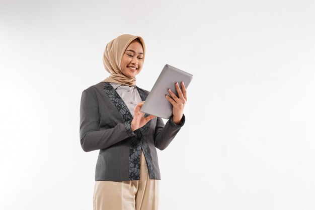 Una mujer con hijab y blazzer gris de pie mirando la tableta