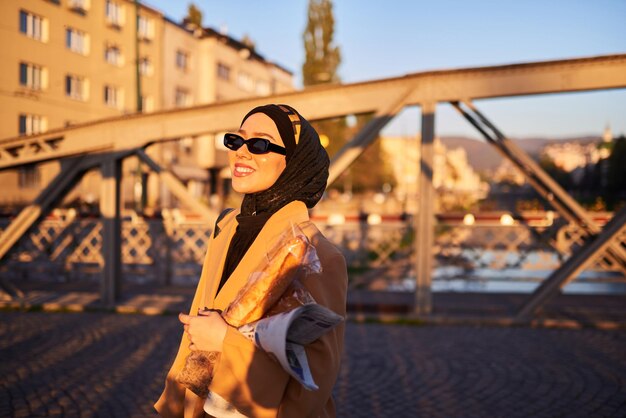 Una mujer en hijab con elegantes gafas de sol y un elegante traje francés caminando por la ciudad al atardecer