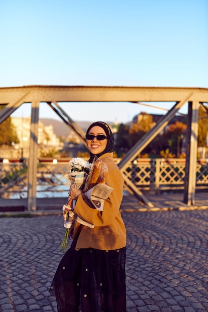 Una mujer en hijab con elegantes gafas de sol y un elegante traje francés caminando por la ciudad al atardecer