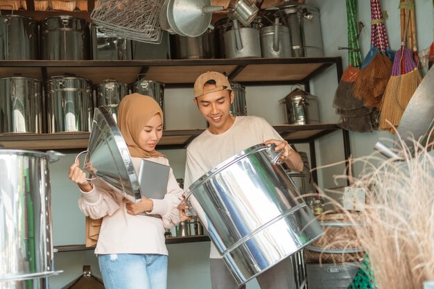 Mujer hijab está usando tableta cuando se abre la tapa grande con el vendedor masculino sosteniendo una gran sartén en la tienda de electrodomésticos